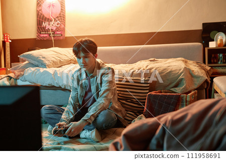Portrait of teen boy holding gamepad and playing videogames sitting on floor at home, copy space 111958691