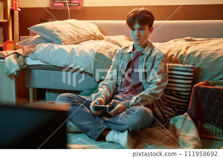 Portrait of teenage boy playing videogames sitting on floor at home, copy space Portrait of teenage boy playing videogames sitting on floor at home, copy space 111958692