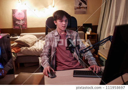 Wide angle view of teenage boy speaking to microphone while live streaming videogames and streaming 111958697