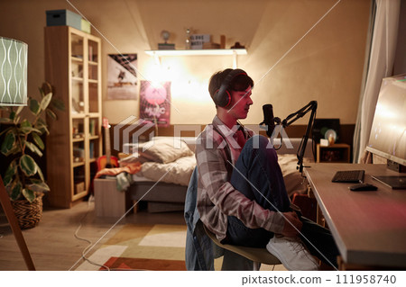 Wide angle side view of teenage boy speaking to microphone while live streaming videogames or vlogging 111958740