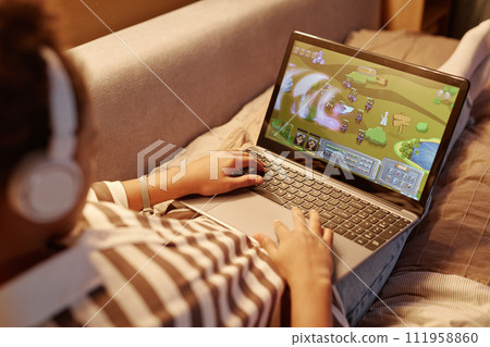 Close up of unrecognizable teenager playing online video games via laptop while lying on bed at night Close up of unrecognizable teenager playing online video games via laptop while lying on bed at night 111958860