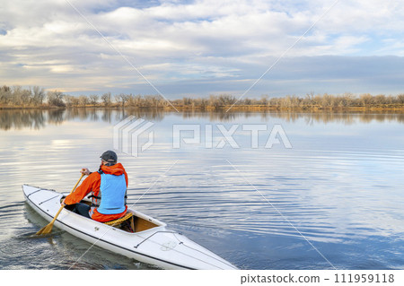 senior male paddler is paddling a decked expedition canoe on a calm lake in northern Colorado, winter scenery without snow 111959118