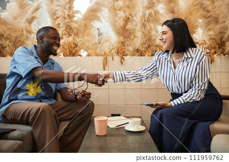 Side view portrait of two smiling business people shaking hands greeting each other during business meeting in office lounge Side view portrait of two smiling business people shaking hands greeting each other during business meeting in office lounge 111959762