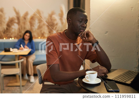 Side view portrait of pensive African American man using laptop in coffee shop and looking at computer screen in cozy low light copy space 111959811
