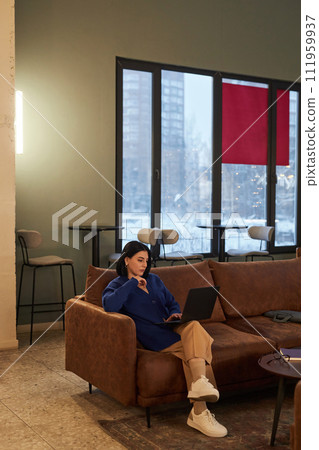 Vertical wide angle view at young businesswoman using laptop sitting on couch in coworking office 111959937