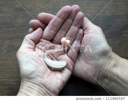 Hearing aid in hands, small electronic device that person wears behind the ear. World hearing day Hearing aid in hands, small electronic device that person wears behind the ear. World hearing day 111960587