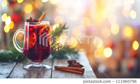 A glass of aromatic red hot mulled wine with cinnamon, orange and muscat, on wooden table with lamps and christmas tree at the background A glass of aromatic red hot mulled wine with cinnamon, orange and muscat, on wooden table with lamps and christmas tree at the background 111960796