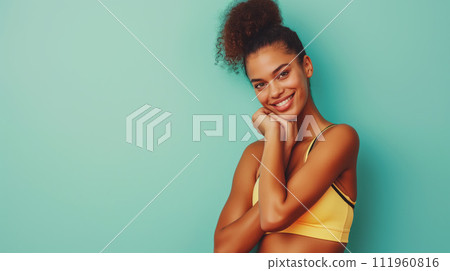 Girl fitness trainer portrait, yellow sport cloth and dark hair smiling and poses in a shy pose, isolated on solid light blue background Girl fitness trainer portrait, yellow sport cloth and dark hair smiling and poses in a shy pose, isolated on solid light blue background 111960816