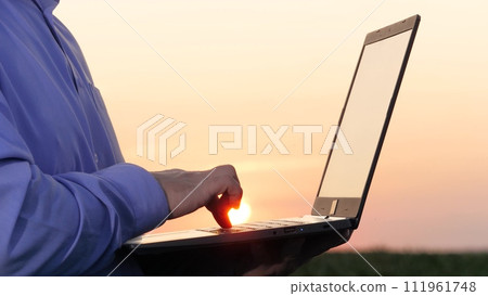 Talented farmer types on laptop working in corn field closeup. Competent peasant grows corn with computer technology at countryside. Efficient agronomist saves data on laptop examining corn field 111961748