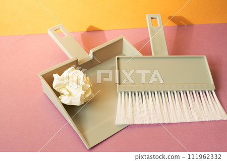 Gray plastic broom brush with dustpan on pink floor. orange wall background Gray plastic broom brush with dustpan on pink floor. orange wall background 111962332