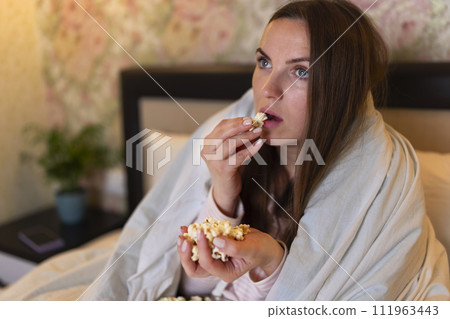 Young woman watching movie on TV in the bed and eating popcorn 111963443