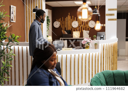 Young African American man tourist waiting for receptionist in reception area, arriving at hotel. Black guy traveler with suitcase standing at empty front desk, wait for check in procedure Young African American man tourist waiting for receptionist in reception area, arriving at hotel. Black guy traveler with suitcase standing at empty front desk, wait for check in procedure 111964682