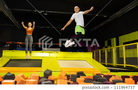 Happy athletes, man and girl, training to jump on trampolines at trampoline center Happy athletes, man and girl, training to jump on trampolines at trampoline center 111964737