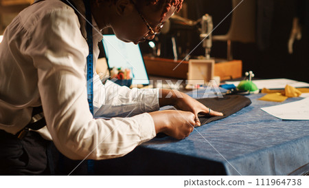 Tailor measuring fabric in workshop, checking material measurements, custom made clothing line. Employee working on luxury fashion collection in fashion atelier. Handheld shot. Close up. Tailor measuring fabric in workshop, checking material measurements, custom made clothing line. Employee working on luxury fashion collection in fashion atelier. Handheld shot. Close up. 111964738
