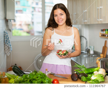 Young woman eating vegetable salad in kitchen 111964767