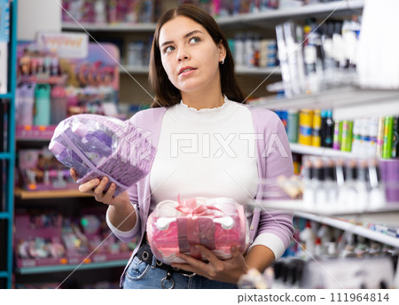 Smiling woman holds two sets of skin and haircare products in her hands during purchases in cosmetic boutique Smiling woman holds two sets of skin and haircare products in her hands during purchases in cosmetic boutique 111964814