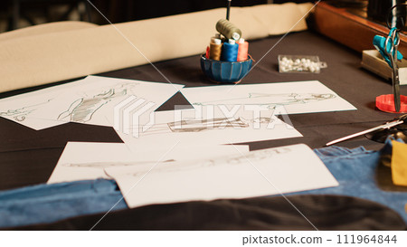 Empty atelier with clothes sketches on papers, modern clothing line and tailoring equipment. Industrial tools and sewing machine used in textile industry. Small business sewing shop. Close up. Empty atelier with clothes sketches on papers, modern clothing line and tailoring equipment. Industrial tools and sewing machine used in textile industry. Small business sewing shop. Close up. 111964844