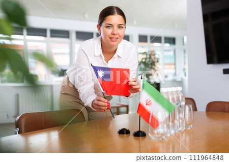 Positive young woman putting little flag of Taiwan on table next to the flag of Iran 111964848