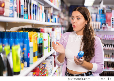 Woman attentively looking hair spray at cosmetics showroom 111964917