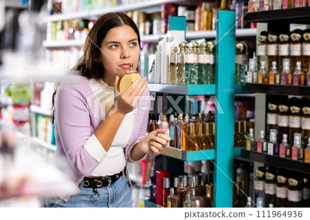 Girl with testers in perfumery, choosing perfume in cosmetic shop Girl with testers in perfumery, choosing perfume in cosmetic shop 111964936
