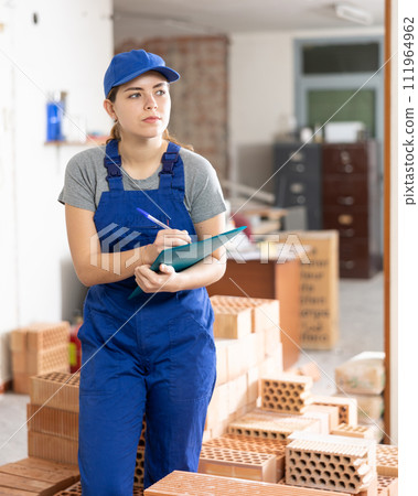 Female designer in blue overalls with papers planning building overhaul Female designer in blue overalls with papers planning building overhaul 111964962