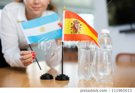 Young woman putting flags of Argentina and Spain on table in office 111965013