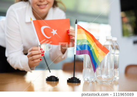 Young woman putting Turkish and LGBT flags on desk in office 111965089