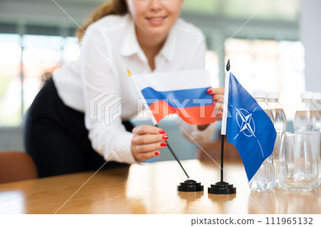 Female secretary places flags of the NATO (OTAN) and Russia on the table before negotiations of top political figures Female secretary places flags of the NATO (OTAN) and Russia on the table before negotiations of top political figures 111965132