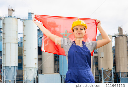 Young female engineer in helmet waving state flag of Morocco while standing in front of big tanks at chemical plant Young female engineer in helmet waving state flag of Morocco while standing in front of big tanks at chemical plant 111965133