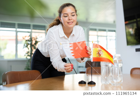 Young woman putting Bahrain and Spain flags on table in office 111965134