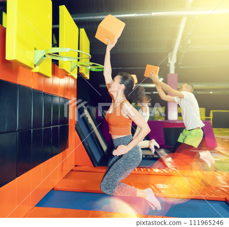 Woman throwing foam cube into basketball hoop at indoor trampoline park Woman throwing foam cube into basketball hoop at indoor trampoline park 111965246
