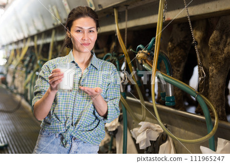 Portrait of a asian farmer woman standing near a milking machine, with a glass of milk 111965247