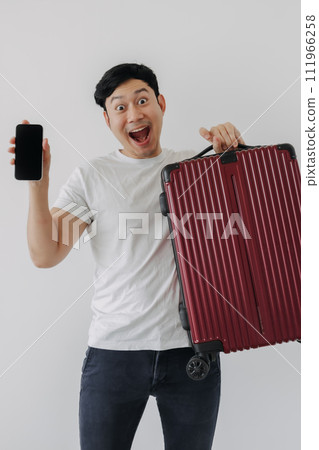Asian man carrying a suitcase and holding mobile phone, showing application for travel and booking. 111966258