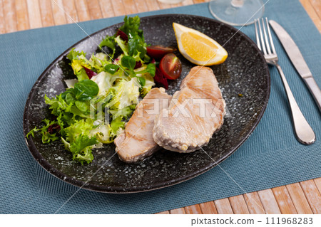 Prepared tuna steak served with lemon and tomato on plate on wooden table 111968283