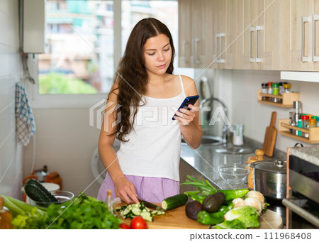 Portrait of woman reading recipe on phone in kitchen 111968408