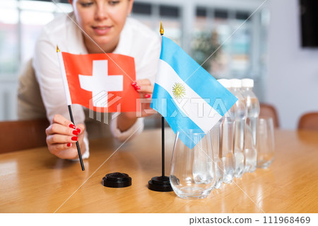 Little flag of Argentina on table and flag of Switzerland put next to it by young woman 111968469