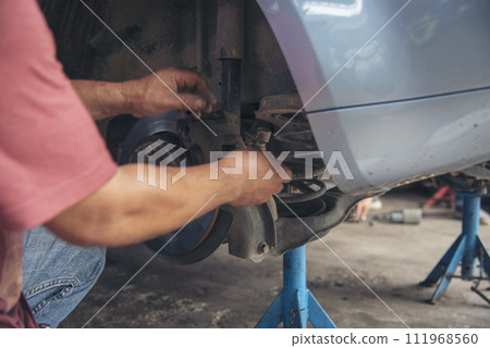 Close up Mechanic man hands repairing car auto repair shop uses jack change tyre. Man hands fixing Shock absorber machinery vehicle mechanical service. Vehicle Car overhaul maintenance engineer Close up Mechanic man hands repairing car auto repair shop uses jack change tyre. Man hands fixing Shock absorber machinery vehicle mechanical service. Vehicle Car overhaul maintenance engineer 111968560