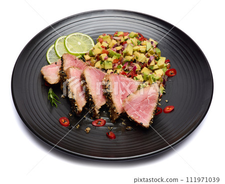 Sliced Organic grilled Tuna fillet covered with sesame seeds and salsa on black ceramic plate 111971039