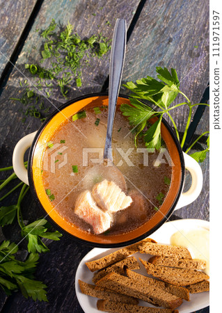 Close-up of a bowl of fish soup with fresh herbs and bread on a wooden table. Close-up of a bowl of fish soup with fresh herbs and bread on a wooden table. 111971597