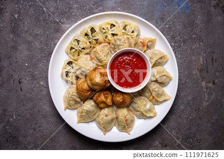 Uzbek samsas and manti with meat, pumpkin and greens on a plate with red sauce 111971625