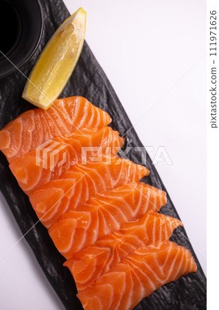 Salmon fillet with lemon and soy sauce on black stone plate, top view close-up. Salmon fillet with lemon and soy sauce on black stone plate, top view close-up. 111971626