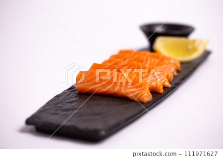 Freshly sliced salmon fillet isolated on a black stone plate with soy sauce and lemon wedge 111971627