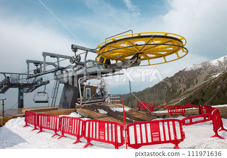 Yellow and gray ski lift wheel and tower with a blue sky and snow-capped mountains in the background Yellow and gray ski lift wheel and tower with a blue sky and snow-capped mountains in the background 111971636