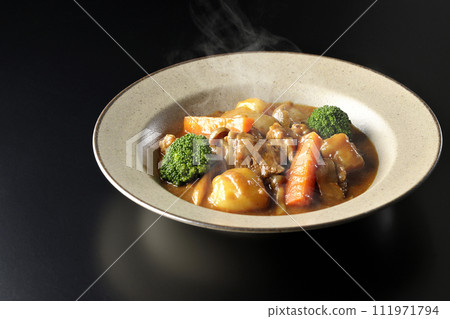 A photo of piping hot beef stew with many ingredients such as broccoli, carrots, and shimeji mushrooms against a black background. 111971794
