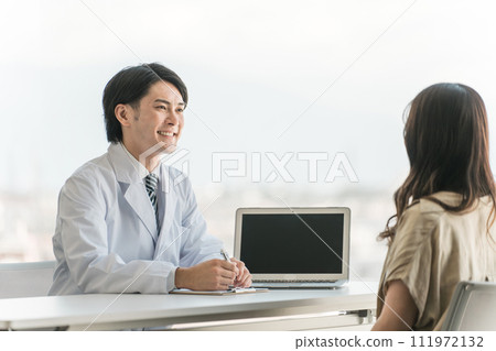 A male doctor who interviews, explains, and examines a female patient in a hospital examination room. 111972132