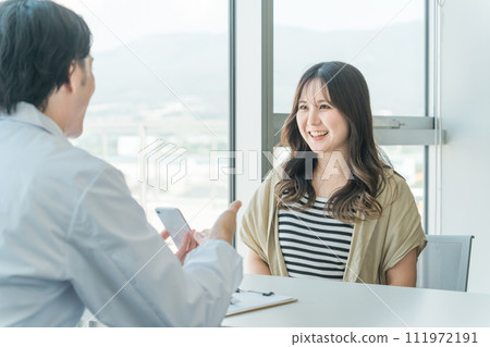 A woman receiving online medical treatment, smartphone examination, remote medical treatment, online examination, and medication guidance from a doctor on her smartphone. 111972191