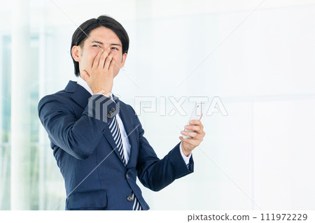 Asian male businessman using a smartphone in the office (troubled, trouble, failure, mistake, what should I do, sympathy) 111972229