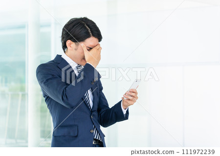 Asian male businessman looking at smartphone in office (failure, mistake, trouble, despair, crying) Asian male businessman looking at smartphone in office (failure, mistake, trouble, despair, crying) 111972239