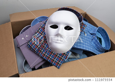 A white mask lies on shirts in an open cardboard box, a concept on the theme of counterfeit products and smuggling A white mask lies on shirts in an open cardboard box, a concept on the theme of counterfeit products and smuggling 111973554
