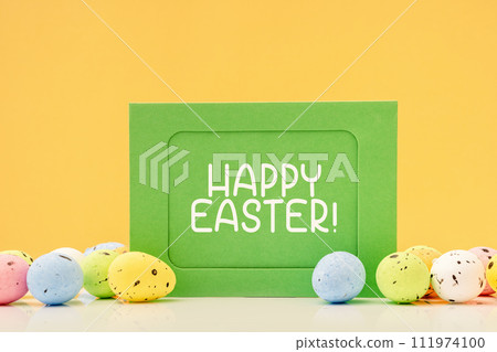 Happy Easter text on green mockup card with eggs and sweets on yellow. Copy space Happy Easter text on green mockup card with eggs and sweets on yellow. Copy space 111974100